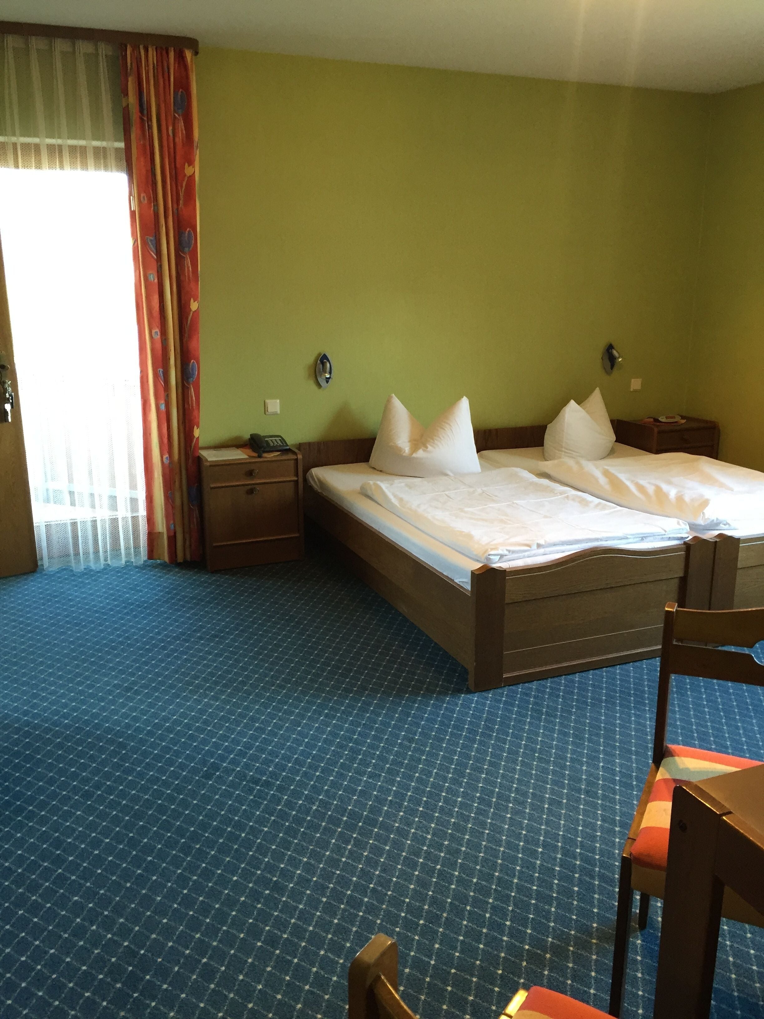 Een hotelkamer met een groot bed, twee nachtkastjes, een stoel en een raam met gordijnen.