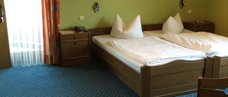 Een hotelkamer met een groot bed, twee nachtkastjes, een stoel en een raam met gordijnen.
