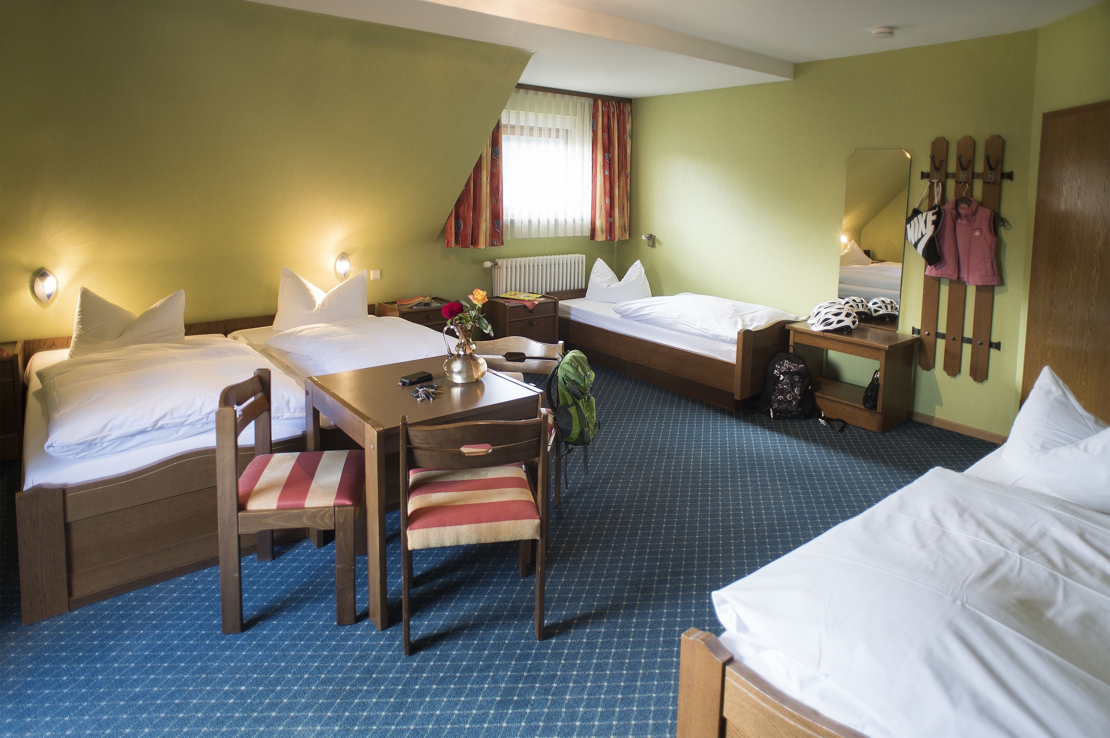 A hotel room with two beds, a desk, a chair, a mirror, and a coat rack.