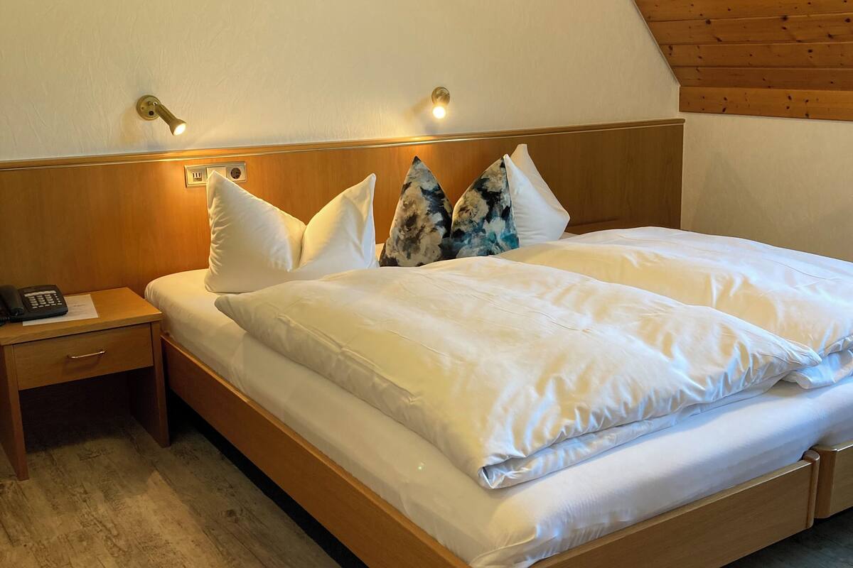 A bedroom with a wooden headboard, a wooden nightstand with a telephone, and a bed with white bedding and decorative pillows.