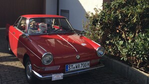 Un coche antiguo rojo estacionado frente a una casa con garaje.