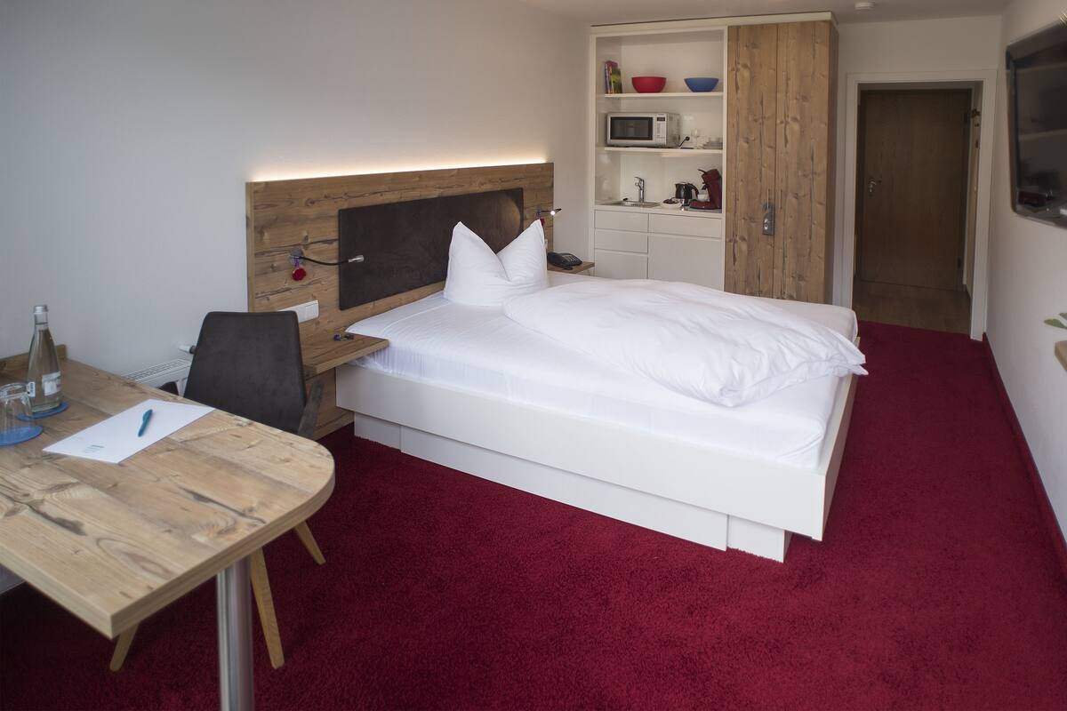 A hotel room with a bed, a desk, a chair, a microwave, and a wardrobe.