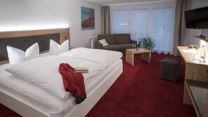 Una habitación de hotel con una cama grande, un sofá, una mesita, un televisor y una alfombra roja.