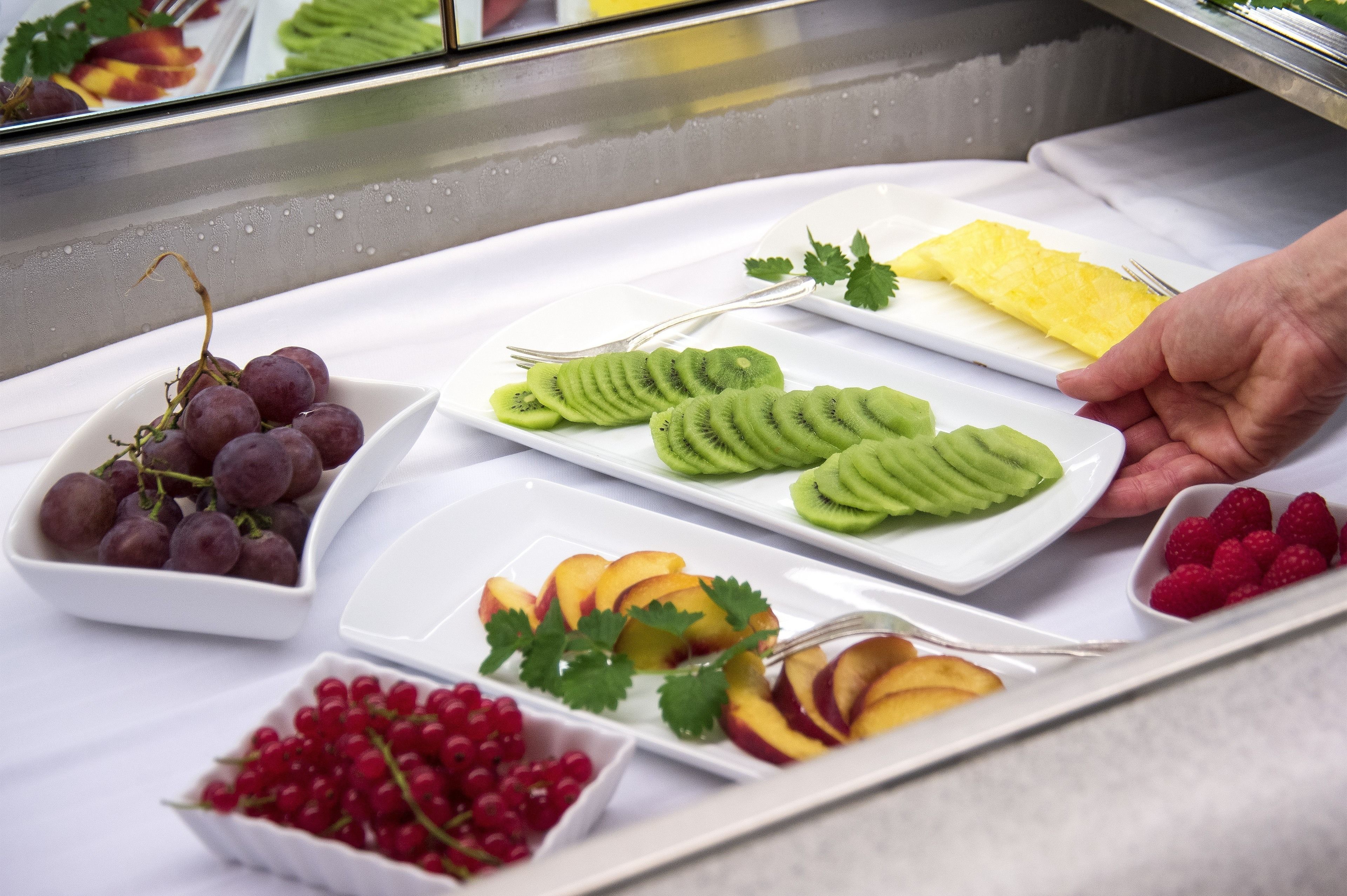 A buffet with various fruits and a hand reaching for a slice of kiwi.