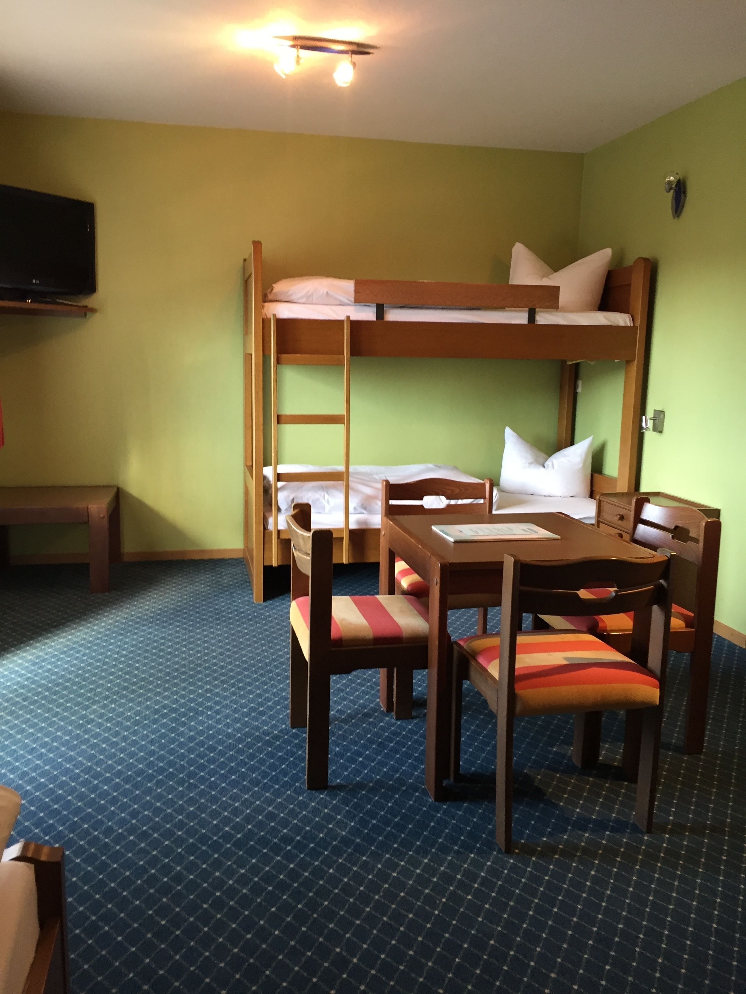 A bunk bed room with a desk and chairs, a television, and a patterned carpet.
