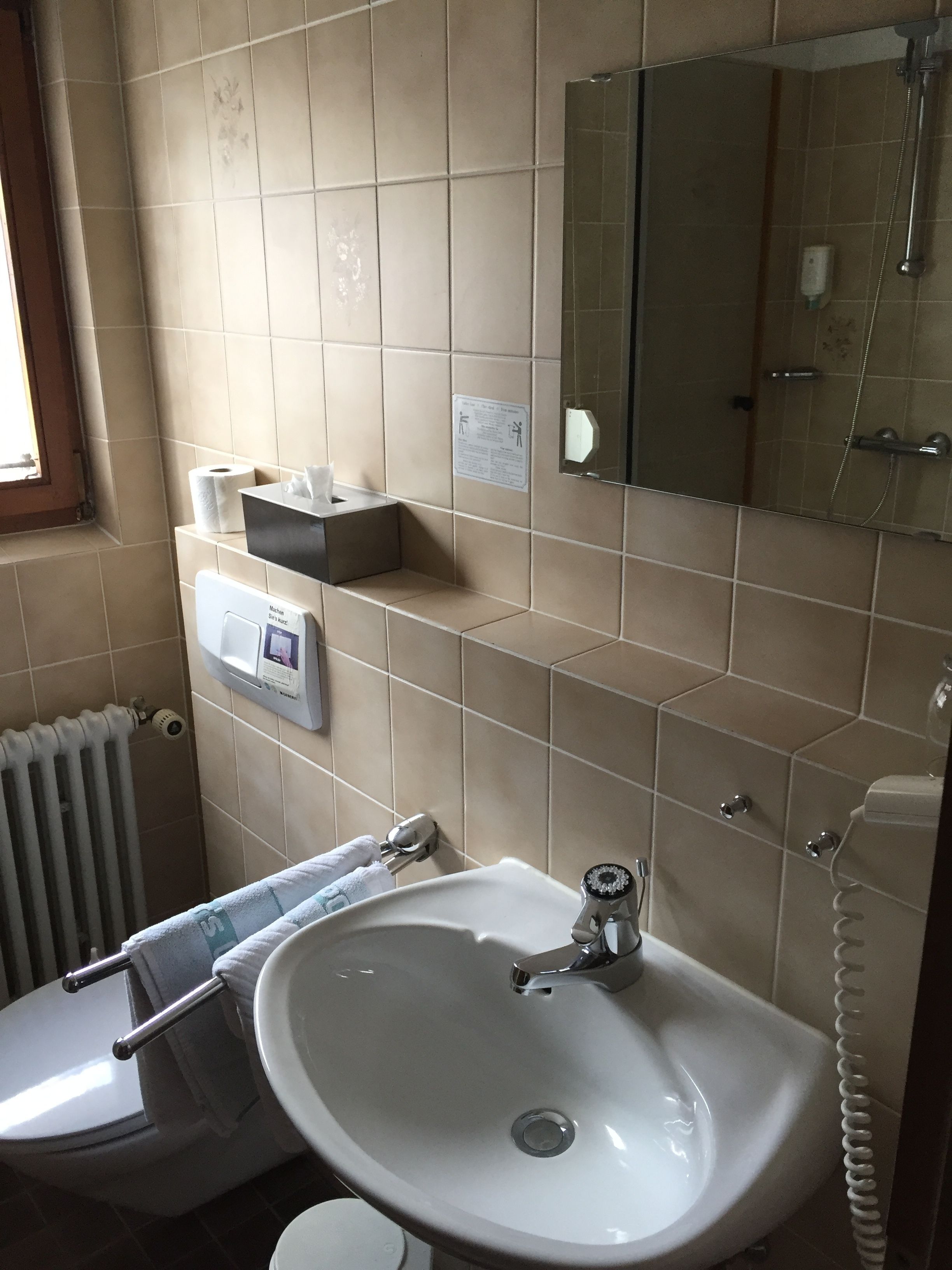 Un baño con lavamanos blanco, inodoro, espejo y dispensador de toallas.
