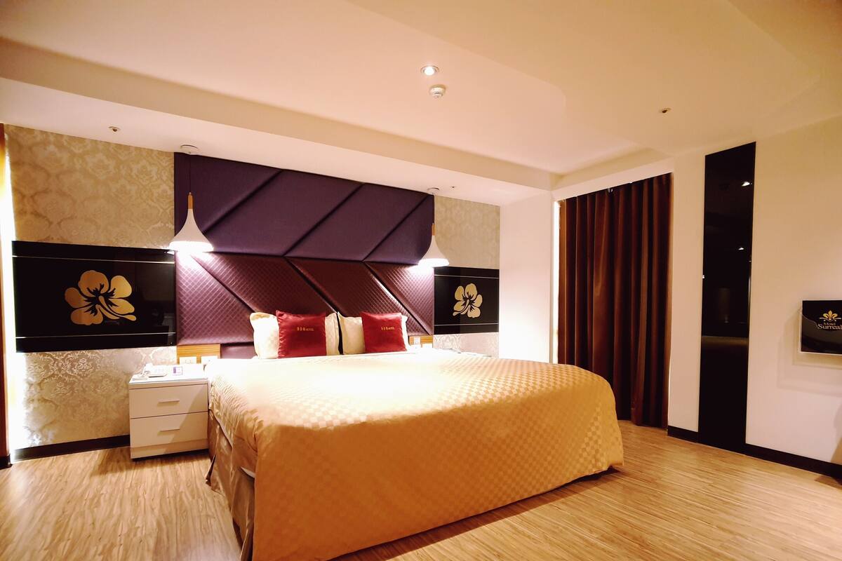Une chambre d’hôtel moderne, dotée d’un grand lit, d’une table de chevet, d’une commode et d’un téléviseur fixé au mur.