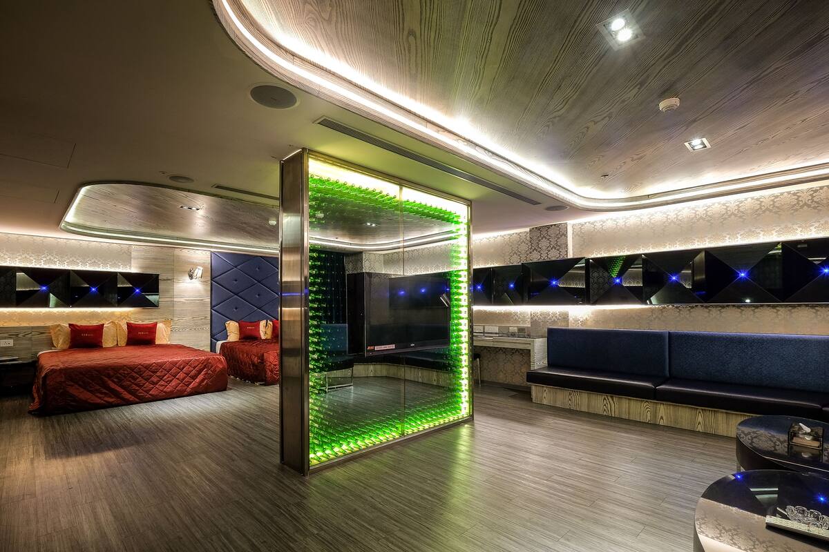 Une chambre d’hôtel moderne dotée d’un grand lit, d’un coin salon et d’une cloison originale illuminée de lumière verte.