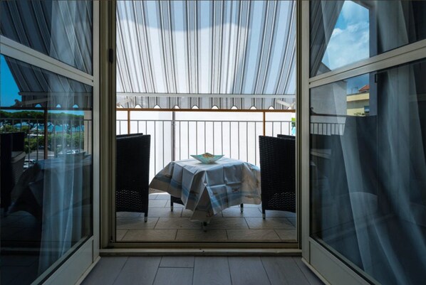 Une véranda fermée par des baies vitrées, avec une table et des chaises, offrant une vue sur l’extérieur.