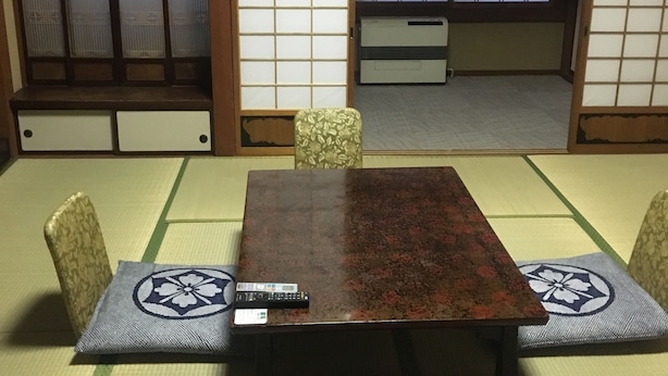 A tatami mat room with a wooden table and chairs, a remote control on the table, and a sliding door with shoji screens. - Hotel Kikuya (Kaminoyama)