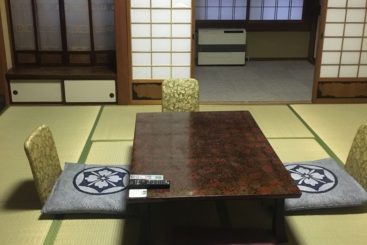 A tatami mat room with a wooden table and chairs, a remote control on the table, and a sliding door with shoji screens.