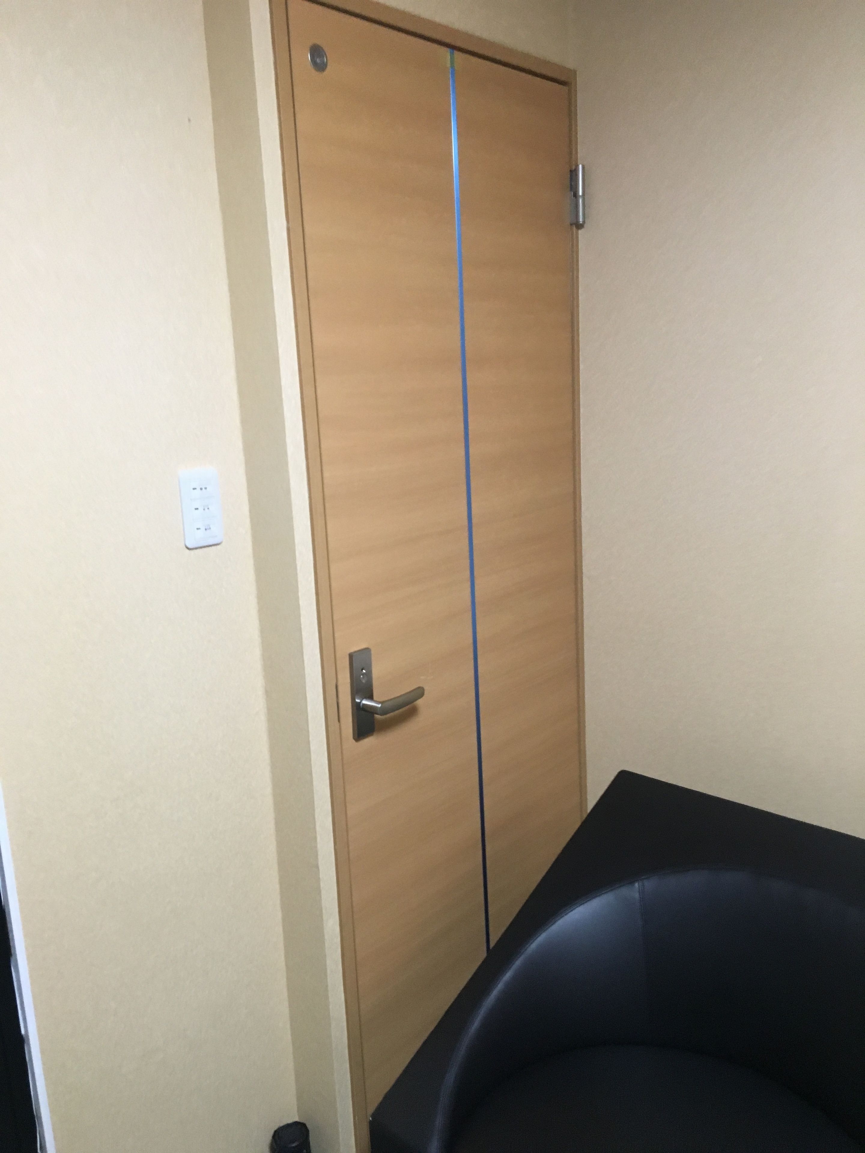 A room with a wooden wardrobe, a black chair, and a wall socket.