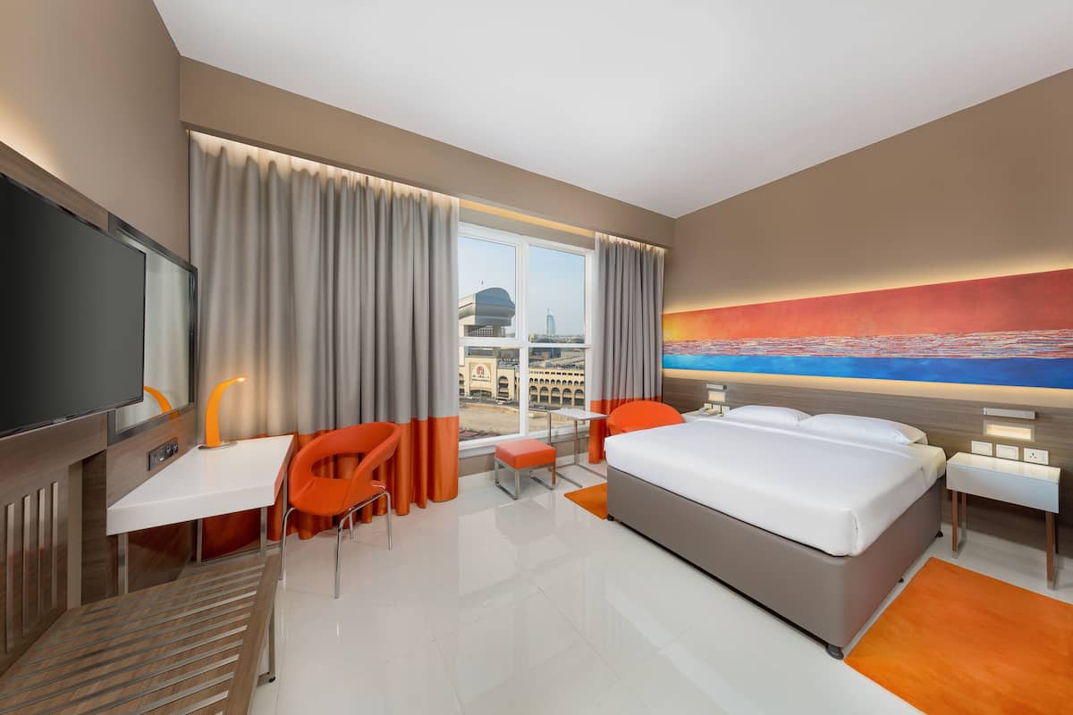 Een hotelkamer met een bed, een bureau, een stoel, een televisie en een groot raam met gordijnen.