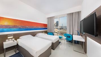 Quarto de hotel com duas camas, uma escrivaninha, uma cadeira, uma televisão e uma janela grande com vista para a cidade.