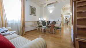 Een ruime woonkamer met een houten vloer, een eettafel met stoelen, een bank en een trap naar een hoger gelegen niveau.