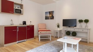 Un salon moderne avec un ensemble de cuisine rouge, un fauteuil blanc, une petite table, un téléviseur et deux plantes en pot.