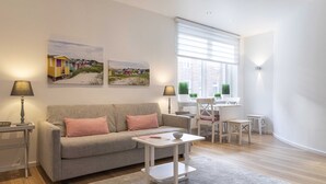 Un salon moderne avec un canapé gris, une petite table blanche et une fenêtre équipée de stores.