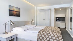 Une chambre d’hôtel avec un lit, une table de chevet, une lampe et un tableau représentant un coucher de soleil sur l’eau.