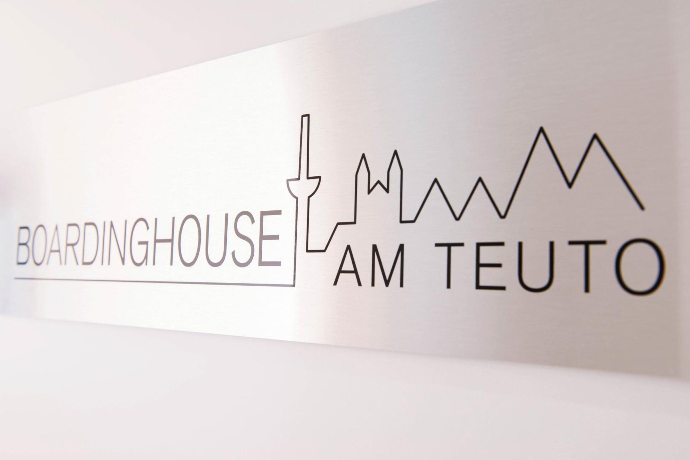 A sign with the text "BOARDINGHOUSE AM TEUTO" and a simple line drawing of a city skyline.