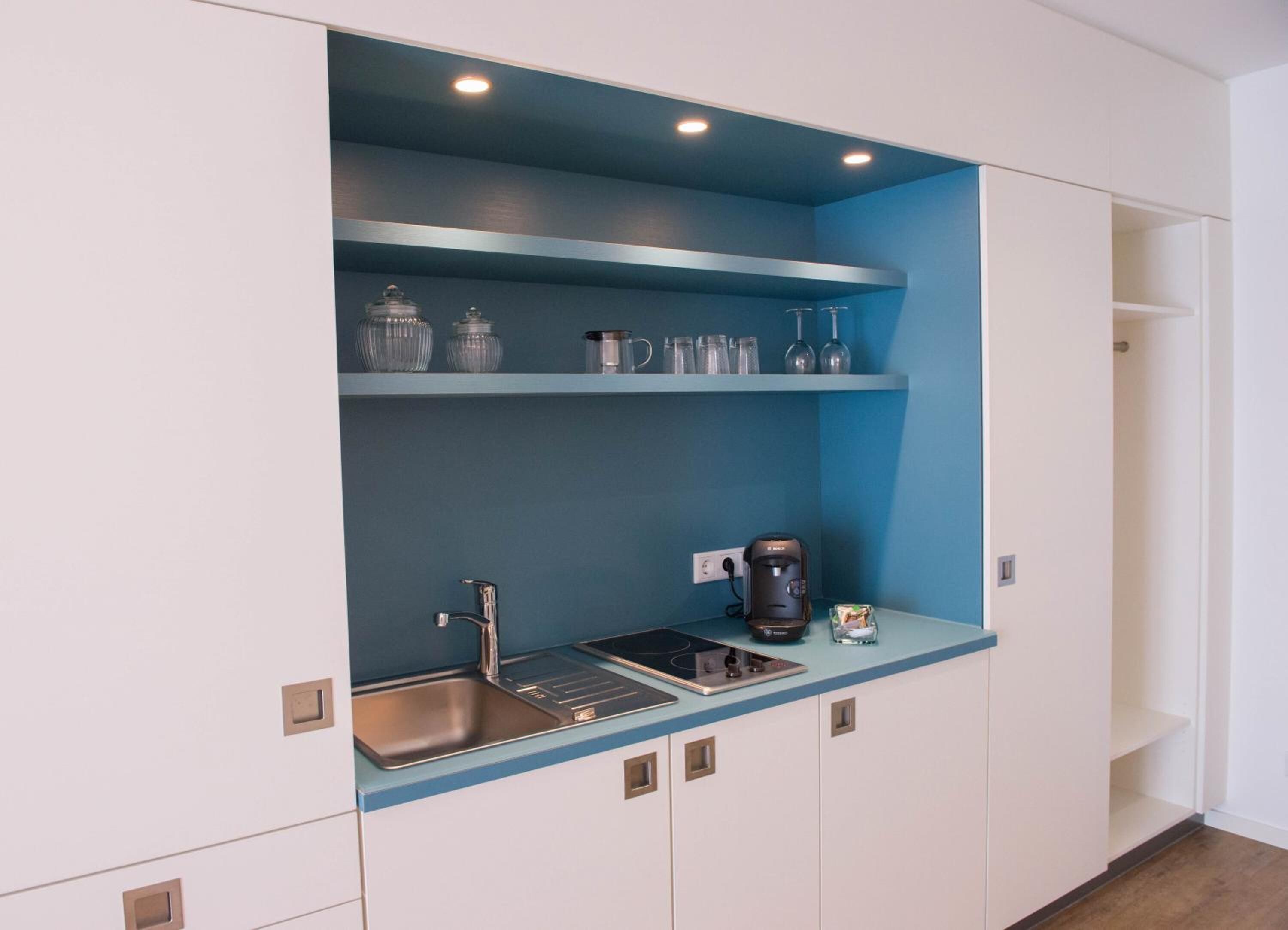 A compact kitchen with a sink, a coffee maker, and glassware on shelves.