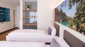 Una habitación de hotel moderna con una cama, un pequeño rincón de descanso, una cocina y un amplio ventanal con vistas panorámicas.