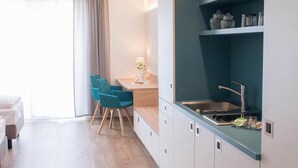 A modern kitchen with a built-in stove, a sink, and a countertop. There is a dining area with a table and chairs. - Apartment - Boardinghouse on Teuto (Lengerich)