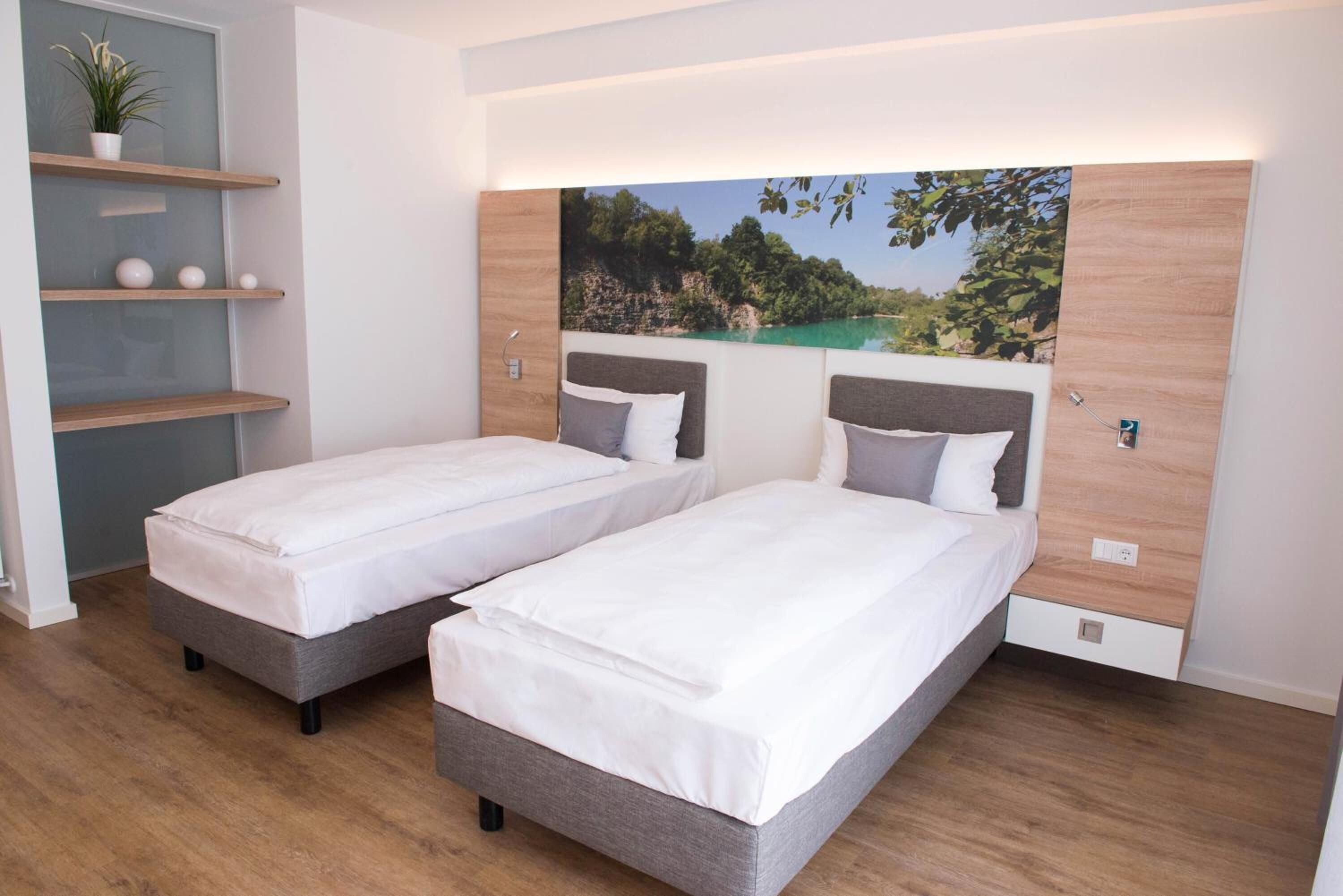 A room with two beds, a wooden floor, a shelf with decorative items, and a large nature-themed painting on the wall.