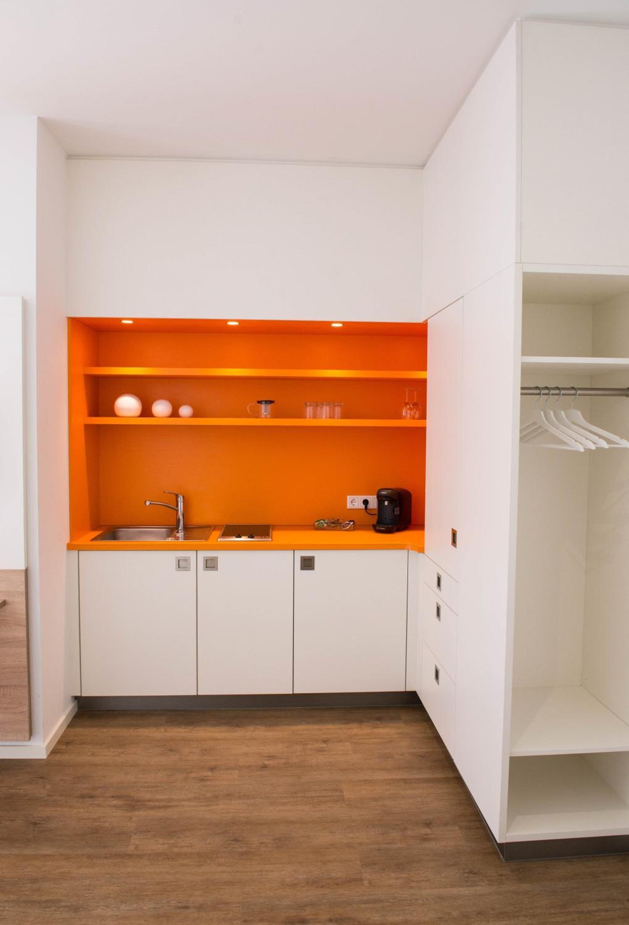 Une cuisine de taille réduite avec des meubles blancs, un plan de travail orange et une machine à café.