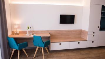 Eine moderne Küche mit integriertem Fernseher, zwei sesseln in Türkisgrün, einer Holz Arbeitsplatte und einem weißen Schrank.
