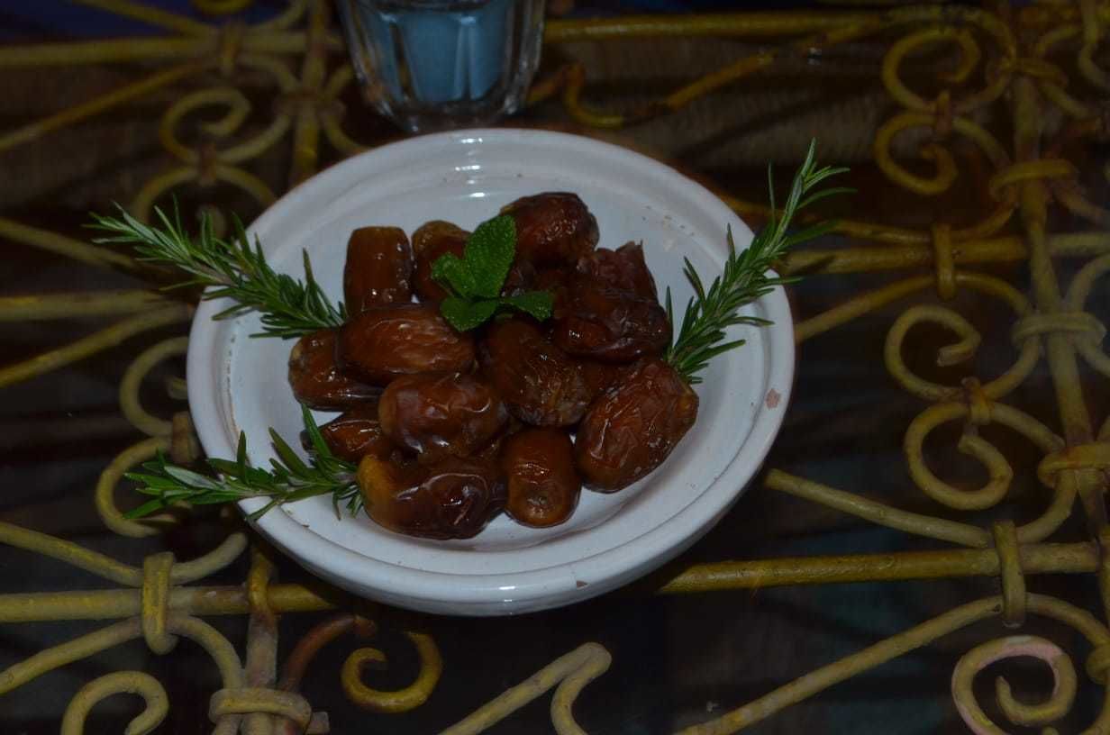 A bowl of dates garnished with rosemary on a table with a decorative metal pattern.