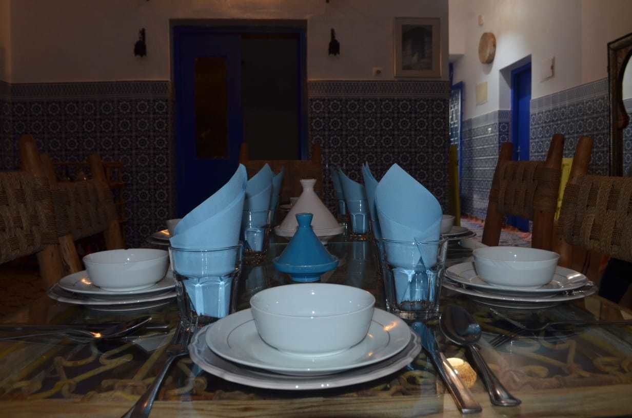 Una mesa de comedor dispuesta con platos blancos, tazones y servilletas azules.