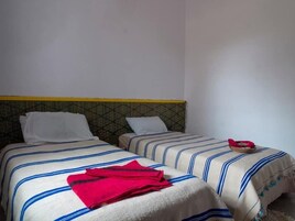 Ein Zimmer mit zwei Betten, jeweils mit gestreifter Bettwäsche und einem Kopfstück mit geometrischem Muster.