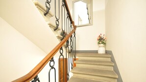 A staircase with a wooden handrail and black metal balusters, leading to a landing with a white vase of flowers. - Ermione (Florence)