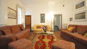 A living room with patterned sofas, a glass coffee table, and a colorful rug. - Ermione (Florence)