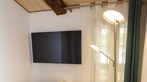 A room with a white sofa, a wooden table, a floor lamp, and a flat-screen TV mounted on the wall. - Relais Des Alpes (Guillaumes)