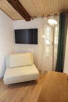 Quarto com sofá branco, mesa de madeira, luminária de chão e televisão de tela plana presa à parede.