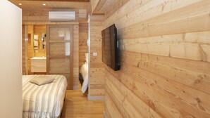 A wooden-paneled room with a bed, a TV mounted on the wall, and a bathroom visible through an open door. - Relais Des Alpes (Guillaumes)