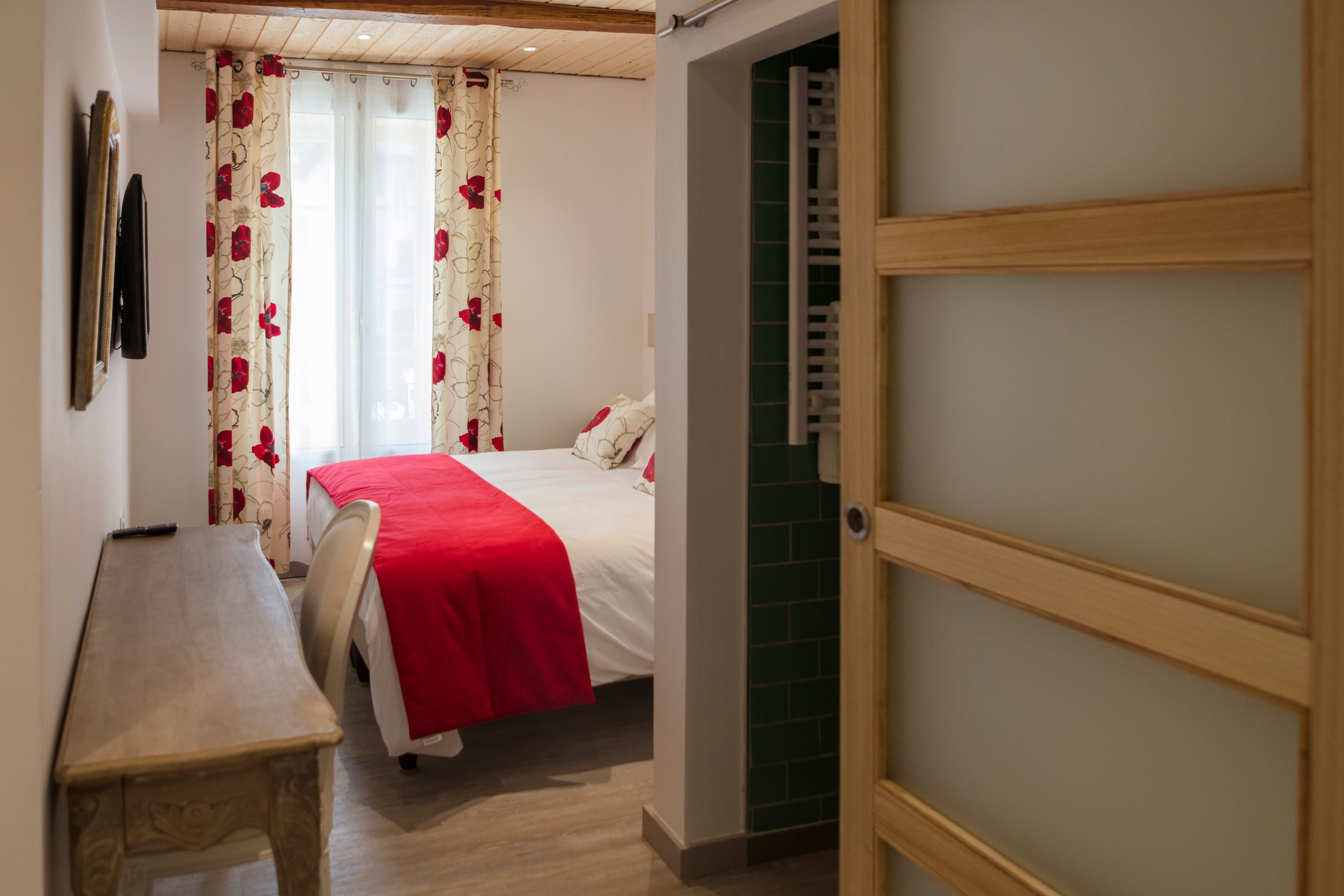 A bedroom with a bed, a desk, and a door leading to another room.