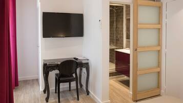 Una habitación con escritorio, silla, televisión y una puerta corredera que da a un baño.