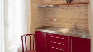 A compact kitchen with a built-in stove, a sink, and red cabinets. - Relais Des Alpes (Guillaumes)
