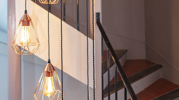 A staircase with a metal railing and three pendant lights with geometric designs. - Relais Des Alpes (Guillaumes)