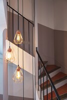 Uma escadaria com corrimão de metal e três luminárias pendentes com designs geométricos.