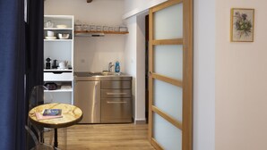 A compact kitchen with a stainless steel refrigerator, a sink, and a wooden cabinet above it. There is a small round table with a book and a cup. - Relais Des Alpes (Guillaumes)