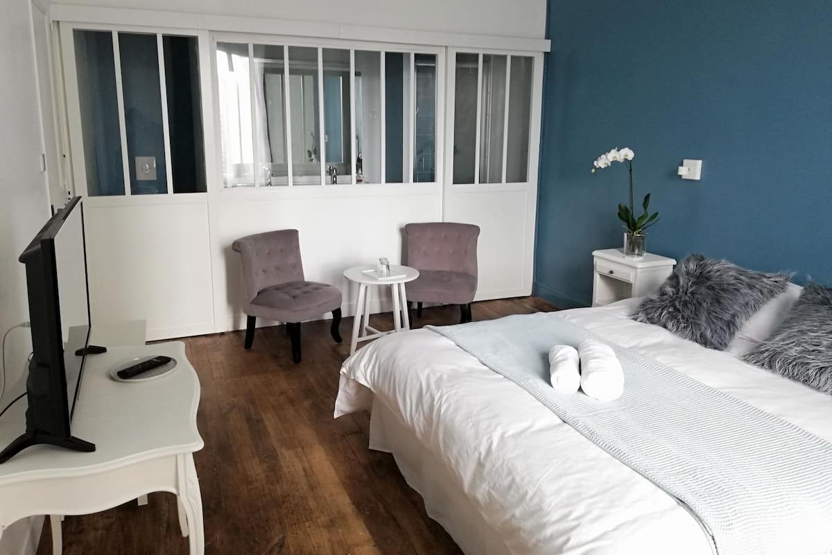 Ein Hotelzimmer mit Bett, zwei Stühlen, einem kleinen Tisch, einem Fernseher und einem Fenster mit Jalousien.