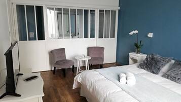 Habitación de hotel con cama, dos sillas, una mesita, televisor y ventana con persianas.