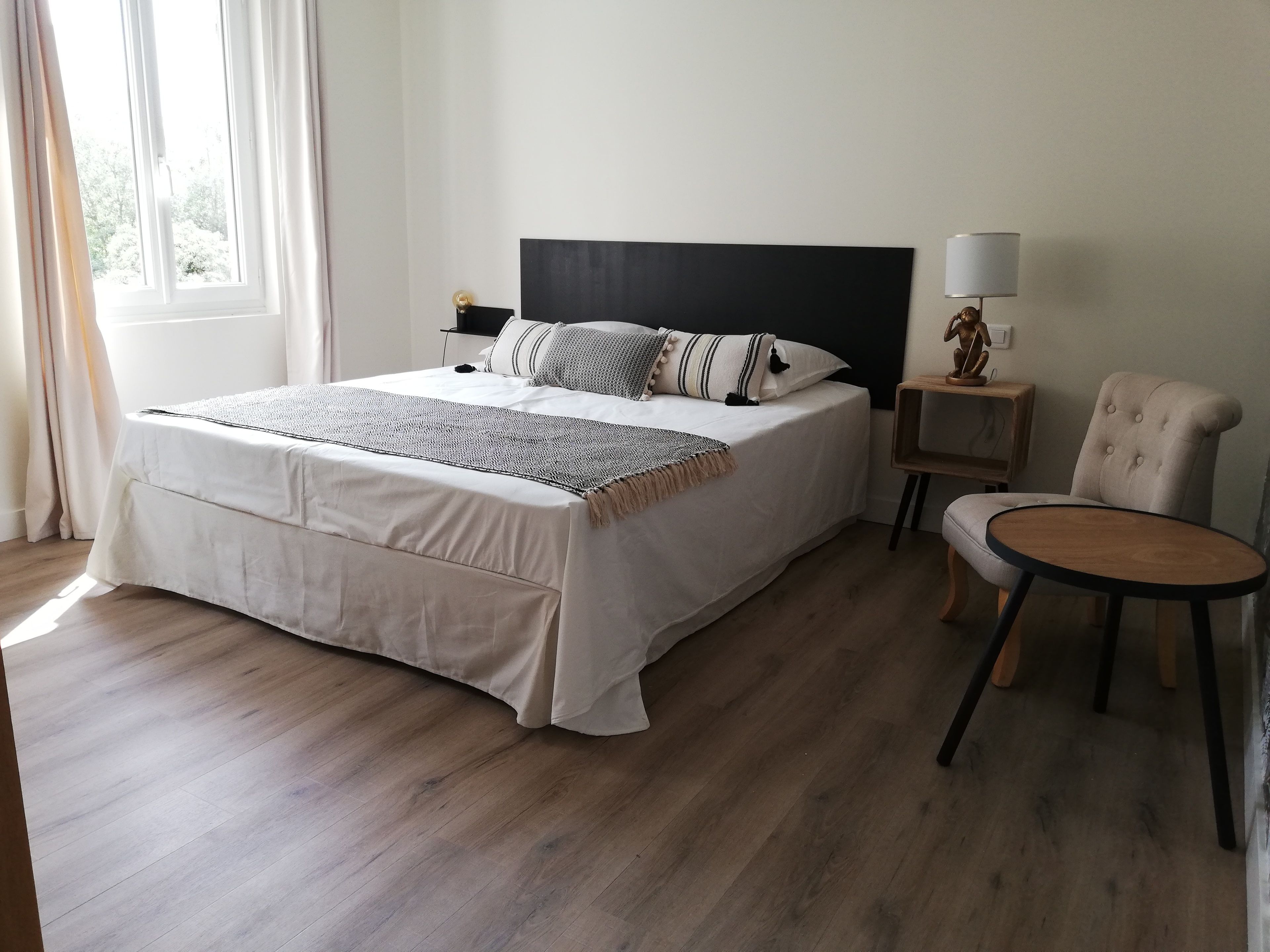 A neatly arranged bedroom with a large bed, a bedside table, a chair, and a lamp.