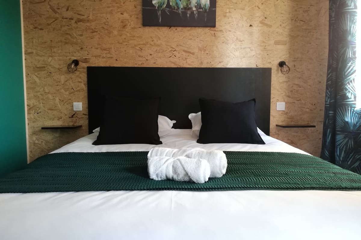 Ein Bett mit weißer Bettwäsche, schwarzen Kissen und einer grünen Tagesdecke.