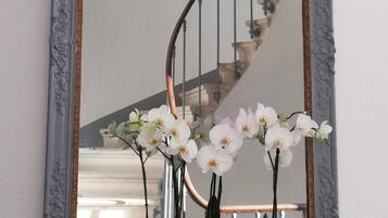 A mirror with an ornate frame reflecting a staircase and a potted orchid plant.