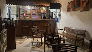 A bar area with wooden furniture, a tiled floor, and a counter with various bottles and a TV screen. - Oasis Wadduwa (Wadduwa)