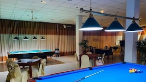A pool table with cues and balls, a billiards table, and a dining area with chairs and a table. - Oasis Wadduwa (Wadduwa)